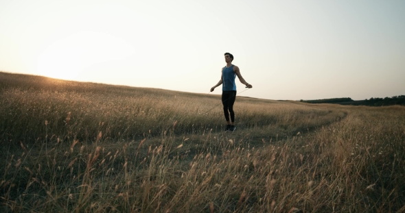 A Young Man in a Sports Suit Who Does Exercises on a Rope for Endurance Kneaded in the Nature on