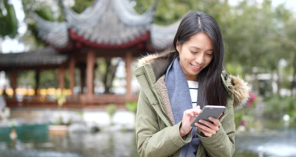 Woman concentrate using cellphone and standing at outdoor Chinese garden 