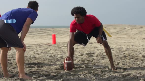 A group of guys playing flag football on the beach.