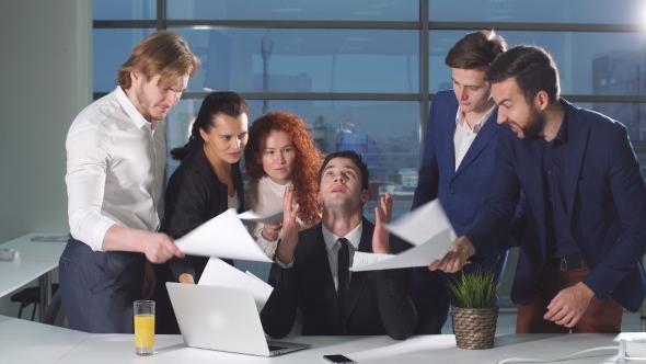 Businessman Under Stress at Work. Colleagues Shaking Papers in His Face.