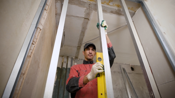 Working Man Is Carefully Levelling Drywall Profiles Using Waterpas.