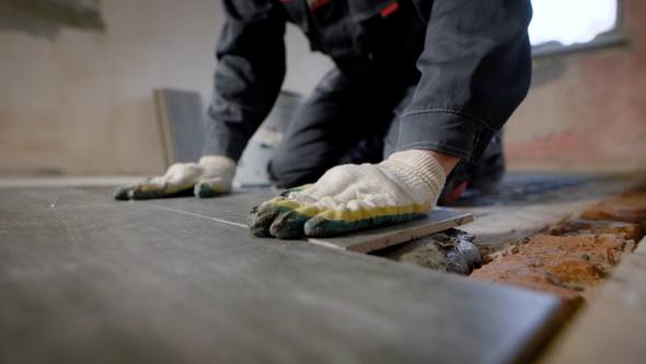 Constuction Worker Laying Down the Tile on Cemented Floor.