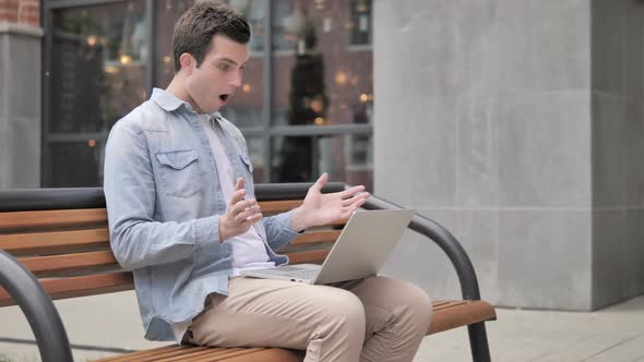 Outdoor Sitting Young Man Shocked By Results on Laptop