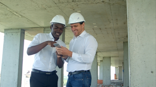 Construction Builders Smiling While Using Smartphone at Site