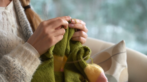 Young Woman Knitting Warm Wool Sweater in the Sitting Room Against Snow Landscape From Outside.