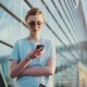 Stylish Young Woman in Trendy Sunglasses Uses Her Mobile Phone, Outside the Glassy Urban Building on - VideoHive Item for Sale