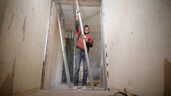 The Builder in Gloves Installs a False Wall, the Man Uses Metal Profiles To Create a Gypsum