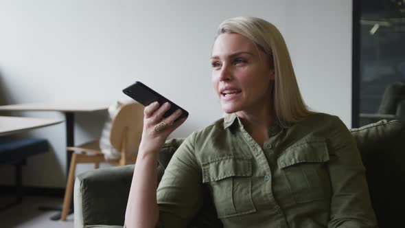 Caucasian businesswoman sitting on couch talking on smartphone in modern office