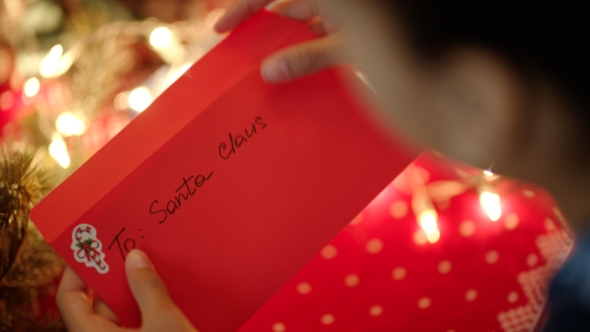 Black Girl Putting a Christmas Letter with Wishlist in the Envelope To Santa Claus on Christmas Eve