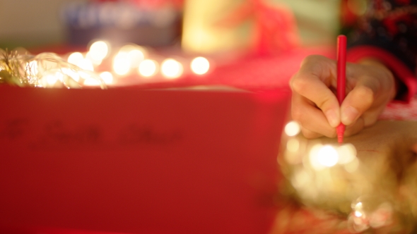 Red Envelope with Santa Claus Address and Hand Writing a Letter on the Background