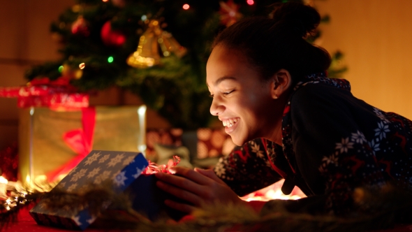 Black Teen Girl Is Openning Christmas Gift Box Under Decorated Christmas Tree