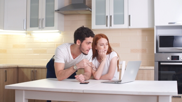 Smiling Couple Standing While Looking at Laptop in Kitchen.