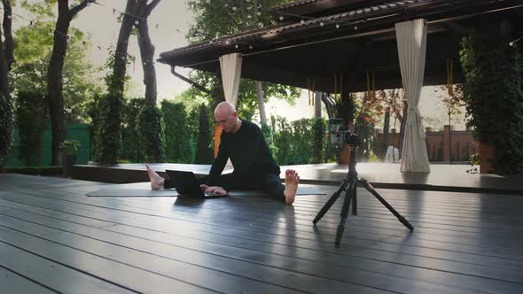 Male in Black Sportswear Practicing Yoga and Typing on Laptop While Sitting on Mat at Veranda