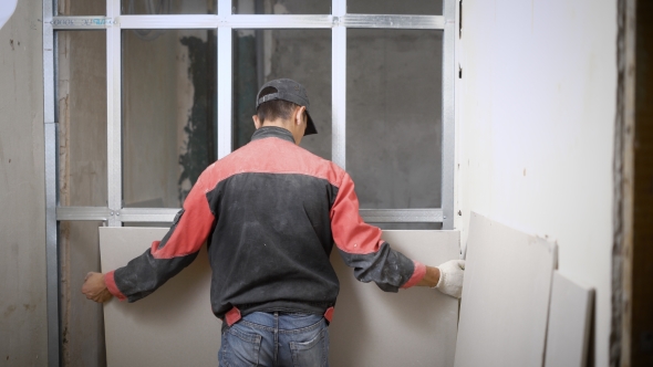 Man Covering Metal Construction of Wall with Panels on Building Site alt