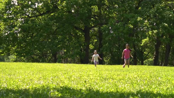 Two Young Asian Girls Running Across the Meadow in the Park Day