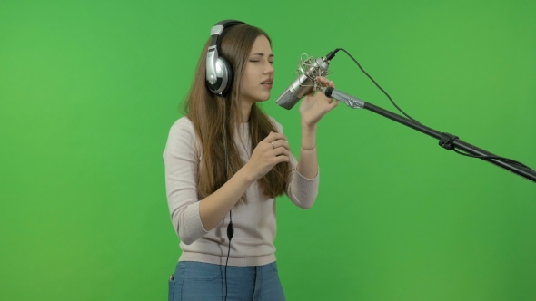 A Young Girl Is Singing Into a Studio Microphone. On a Green Background.