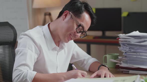 Close Up Of Smiling Asian Man Enjoys Working With Documents At The Office