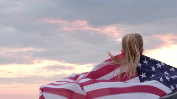 Blonde Girl Running Waving National USA Flag Outdoors Over Sunset Sky at Summer on Beach American