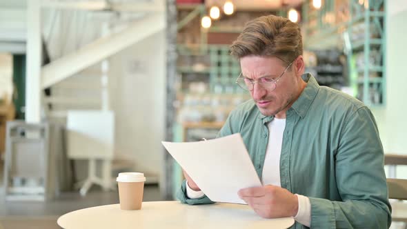 Middle Aged Man Reacting to Loss on Documents in Cafe