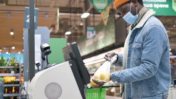 AfricanAmerican Male Customer Wearing a Medical Mask Punches Through Items at a Selfservice Checkout