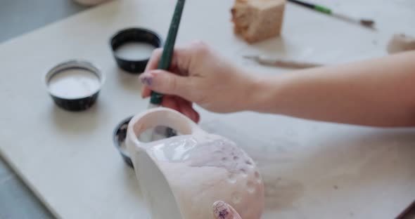 Female Potter Sitting and Stirs Paint with a Brush a Cup on the Table. Woman Making Ceramic Item