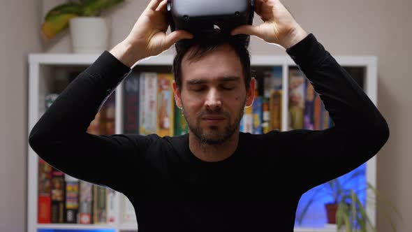 A Caucasian man in a black sweatshirt removes his VR helmet from his head and smiles