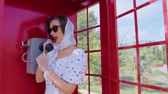 Beautiful Young Woman Happily Speaks on the Phone in an English Style Red Telephone Booth