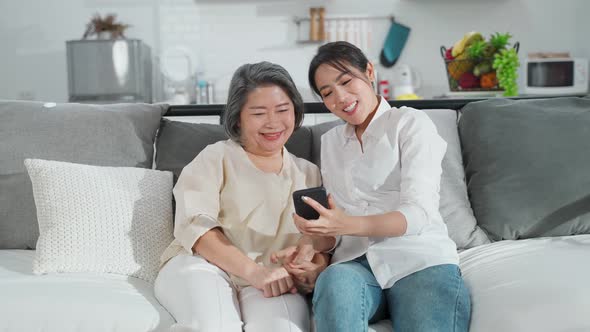 Asian family woman and her mother using smartphone teaching to play internet online together at home