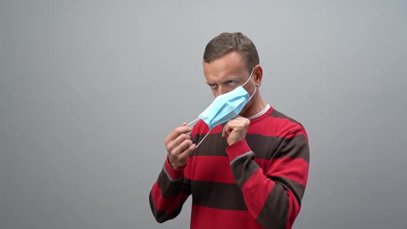 Man Wearing a Grey Shirt Putting on a Mask on a White Background