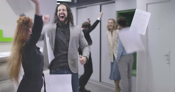 Portrait of Group of Young Office Workers Throwing Papers Up and Jumping. Multiethnic Team