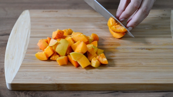 Female Hands Cut Apricot on Wooden Board