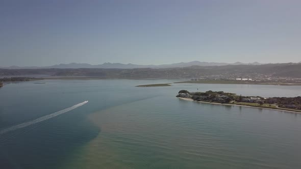 Aerial: Lone power boat turns around in sunny Knysna Lagoon harbour