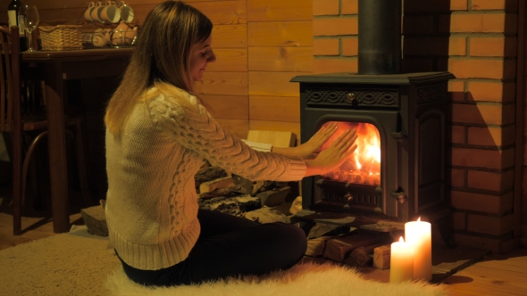 Lovely Woman Sitting On White Fluffy Carpet, Warming His Hands By The Fireplace