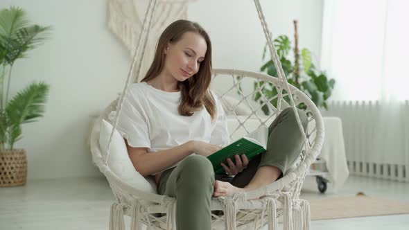 A Woman Reads a Book While Sitting on a Swing at Home