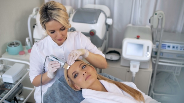 The Cosmetologist Makes the Procedure Ultrasonic Face Peeling of the Facial Skin of a Beautiful