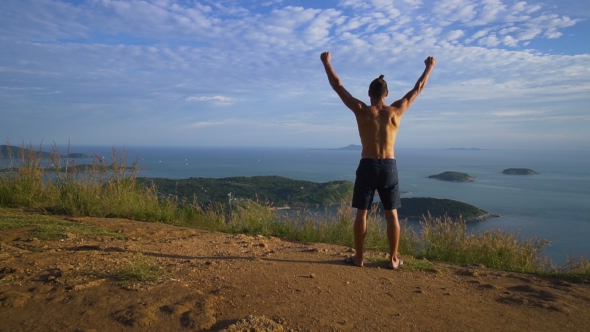 Athletic Young Man Raises His Hands Up Standing on the Edge of the Mountain.