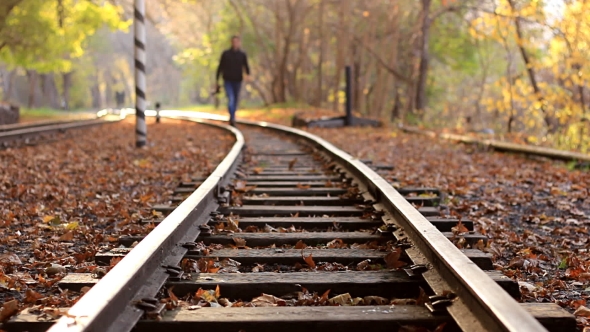 A Man with DSLR Camera Walks Down Train Tracks on a Background Autumn Forest. A Man Approaches the