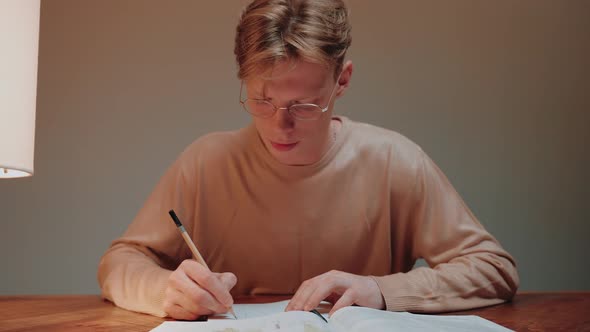 Closeup of Young Man Studying at Home Writing in His Notes Reading a Textbook