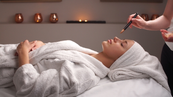 Female Cosmetologist Making Cosmetic Facial Mask To the Female Client at the Cosmetology Centre.