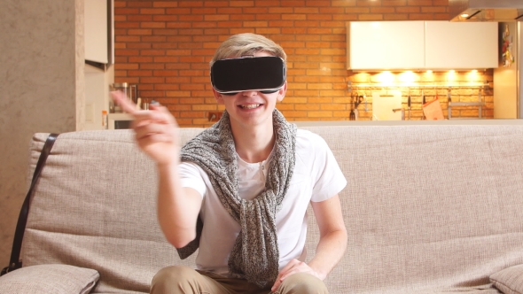 Young Man Uses Virtual Reality Glasses in the House, Leafing Through the Virtual Pages.