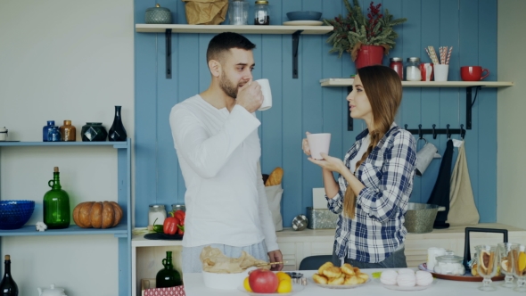 Attractive Couple Talking and Drinking Coffee in the Kitchen in the Morning at Home