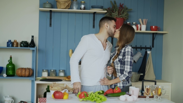 Happy Young Couple in the Kitchen. Attractive Dancing Man Cooking While His Girfriend Come and Help
