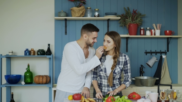 Happy Young Couple in the Kitchen. Attractive Dancing Man Feeding His Girlfriend While She Is