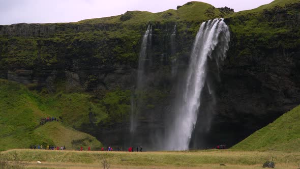 Tourists in Raincoats Near the Waterfall