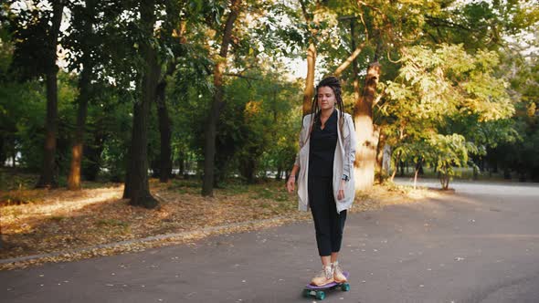 Pretty Young Woman with Dreadlocks Riding Skateboard in Park Slow Motion