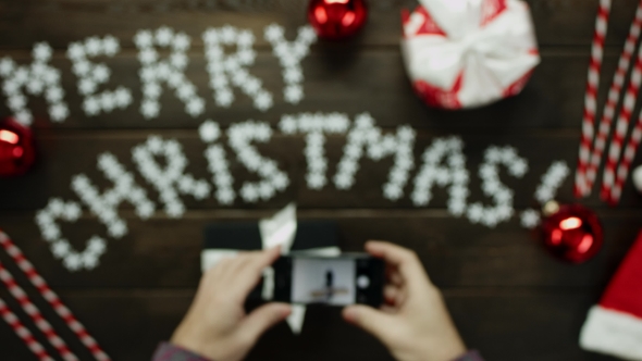 Man Takes Photo of His Christmas Gift on Smartphone Camera on Decorated Christmas Table, Top Down