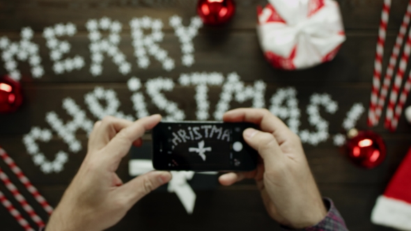 Man Takes Photo of His Xmas Present on Smartphone Camera on Decorated Christmas Table, Top Down Shot