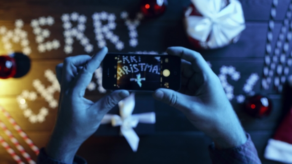 Man Takes Photo of His New Year Present on Smartphone Camera on Decorated Christmas Table, Top Down