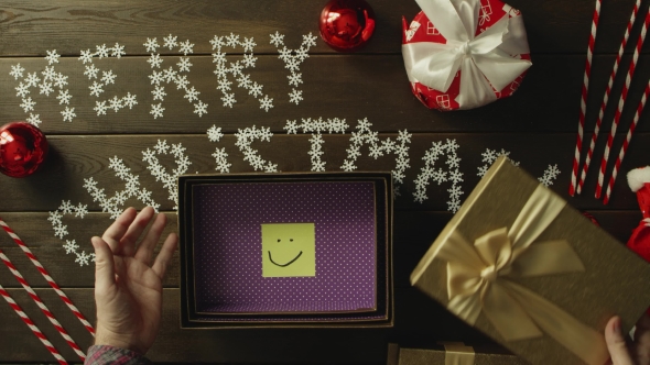 Top Down Shot of Adult Man Opening New Year Gift with Sticky Note with Smile Inside