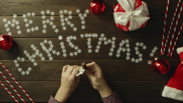 Man Unwraps Candy, Eats It and Throws Wrapper on Christmas Decorated Table, Top Down Shot